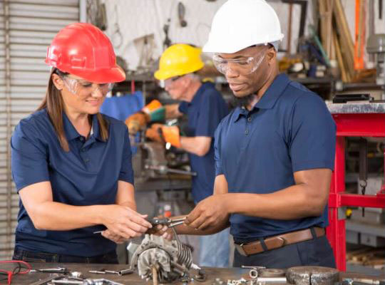 A man and women in hardhats working on a motor.